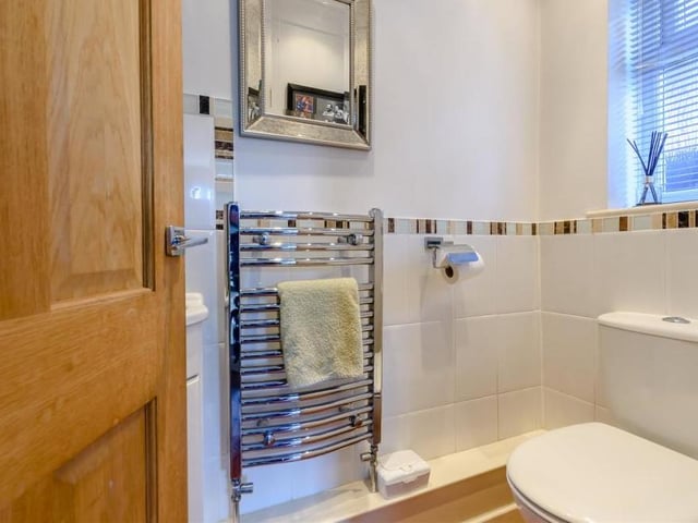 Off the rear lobby, at the far end of the hallway, is this downstairs loo. It comprises a low-flush WC, corner wash hand basin with mixer tap and storage cupboard beneath, chrome, heated towel-rail, part-tiled walls and ceiling spotlights.