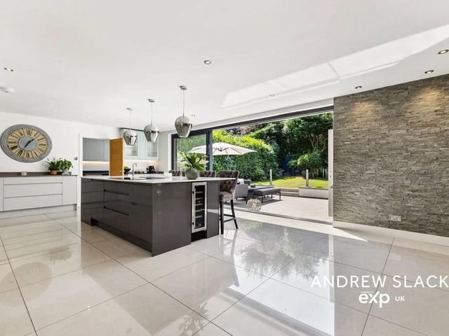 At the heart of the home lies a show-stopping open-plan kitchen/dining/living area with sleek cabinetry, premium appliances, a large central island with integrated wine fridge, and bi-fold doors that open seamlessly onto the private, landscaped garden