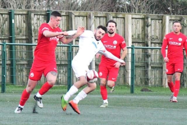 Jaz Goundry of Sherwood Colliery (all red) battles against both Consett AFC and the gale force wind