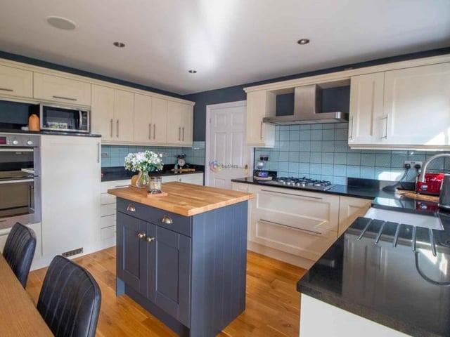 Black granite work surfaces incorporate a Belfast sink and a stainless steel five-burner hob with extractor above. Other kitchen comforts include a stainless steel double oven, next to the larder fridge.