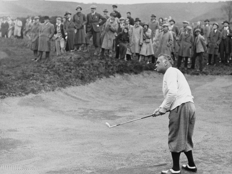 Specatators look on as Cyril Tolley of England, smoking a cigarette, plays a chip shot out of the sand bunker during the English Amateur Golf Championship golf tournament on 2nd May 1935 at the Notts Holinwell Golf Club in Kirkby.