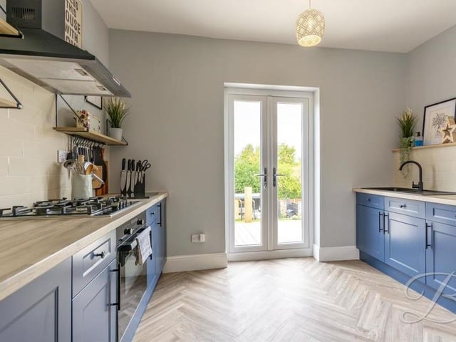 The kitchen/diner from a different angle, showing French doors that lead out to the back garden. There is an integrated oven and a gas hob with extractor fan above, plus an inset sink and drainer with mixer tap.