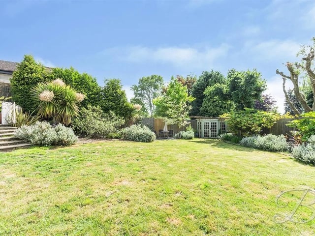 The rear garden offers a variety of patio seating areas, laid lawn and surrounding mature trees and shrubbery.