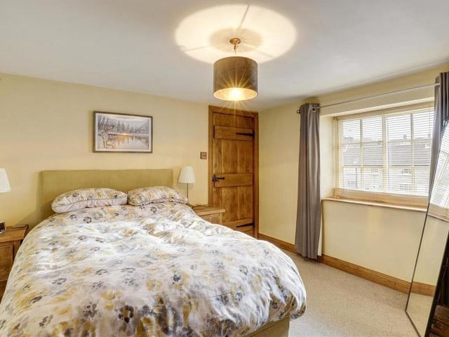 A second shot of the first bedroom, which is bright thanks to a wood-framed sash window. The floor is carpeted.