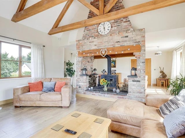 The impressive living room boasts exposed wooden beams and a central exposed brick fireplace with a double-sided log burner, creating a warm and inviting space.