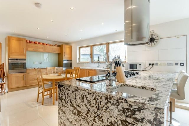 Into the kitchen itself, which features two integrated electric ovens, a six-ring stainless steel gas hob and stainless steel chimney extractor hood above. A large peninsula island includes an additional Belfast sink with mixer tap
