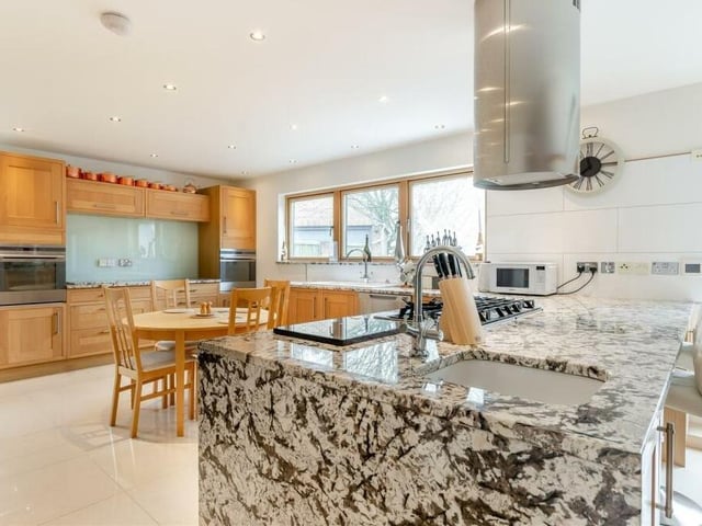 Into the kitchen itself, which features two integrated electric ovens, a six-ring stainless steel gas hob and stainless steel chimney extractor hood above. A large peninsula island includes an additional Belfast sink with mixer tap