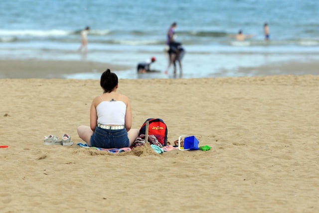 A woman sits on the sand, watching on as people play in the sea at Sandhaven beach.