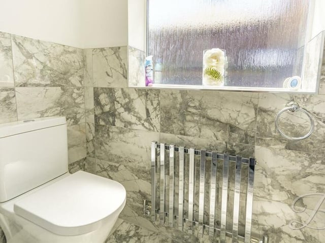 The ground floor of the Kirkby house also includes a handy cloakroom with storage space and access to this contemporary toilet. It comes complete with a low-flush WC, vanity hand wash basin, chrome central heating radiator and half-height marble tiling.
