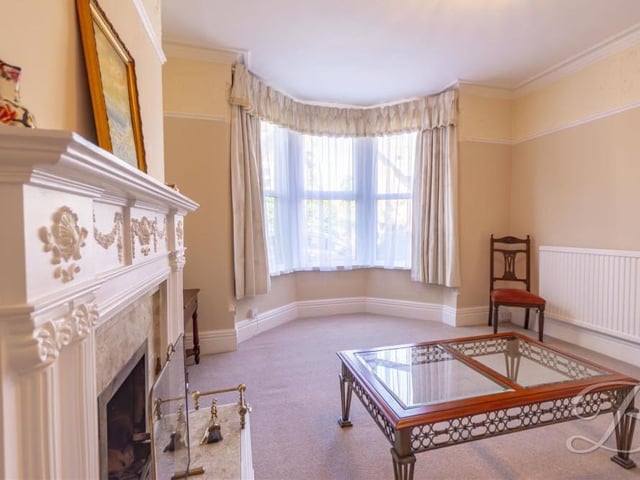A second view of the living room, showing the beauty of the bay window, which overlooks the front of the property. The floor is carpeted, the decor is neutral and there's a central heating radiator.