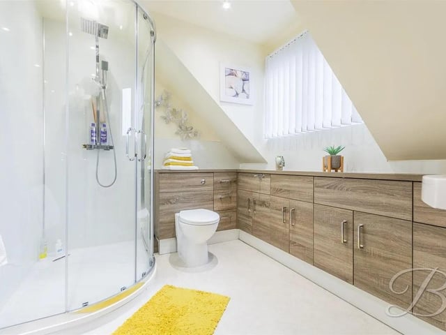 Spacious en suite featuring a large shower cubicle, surrounding cabinets with a hand wash basin, a low-flush WC, and a window to the front elevation.