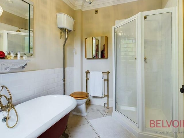 Here is the spacious and fully fitted en suite bathroom to the primary bedroom, A four-piece suite comprises a roll-top bath with mixer tap and shower, hand wash basin, WC and corner shower cubicle with white, tiled walls. A stained glass sash window and light-coloured Karndean flooring complete the look.