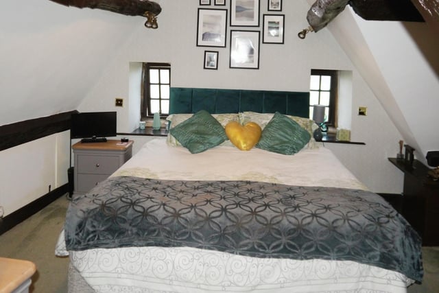 The master bedroom boasts two built-in wardrobes and drawers, wardrobe, as well as a vaulted ceiling with exposed beams.