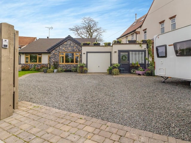 This photo shows the extensive gravel driveway that not only offers off-street parking space but also leads to the integral garage, which is equipped with power and light. You can also see the superb granite wall feature on the outside of the bungalow.