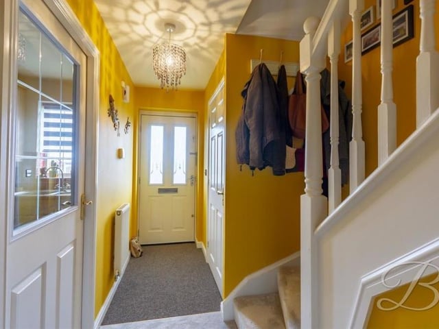 In we go to the Cambourne Place house, finding ourselves in this warm and welcoming entrance hallway, which features a carpeted floor and a central heating radiator. Of the doors pictured, one leads to the kitchen and the other to the downstairs toilet.