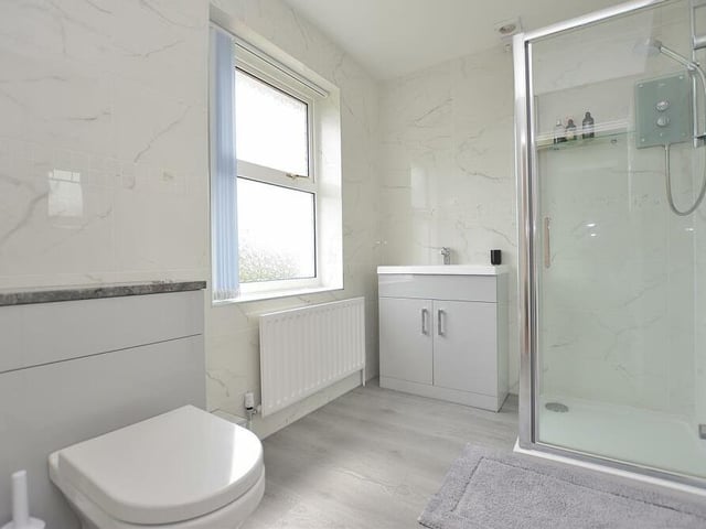 The second bedroom also benefits from a contemporary en suite shower room. It comprises a tiled shower cubicle with an electric Mira shower, a vanity unit with inset wash hand basin and storage cupboard beneath, and a low-flush WC with enclosed cistern. It also boasts a vinyl floor and beautiful marble-effect tiled walls.