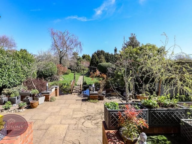 The rear garden features a raised artificial lawn area, stone steps down to the patio area, with a range of well established plants and shrubbery, a timber bridge over a koi fish pond, leading to the expansive turfed lawn, with a range of well established trees, plants and shrubbery, as well as a timber summer house; the garden is palisaded by timber fencing.