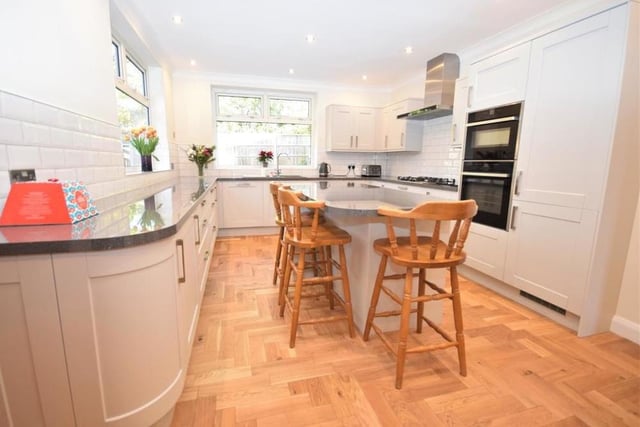 The kitchen from a different angle. High-end fixtures include a double oven, a five-ring gas hob, with extractor above, and dishwasher. The room is finished with tiled splashbacks, practical and smart wood-flooring and a radiator.