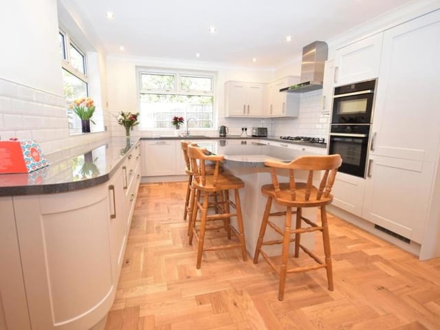 The kitchen from a different angle. High-end fixtures include a double oven, a five-ring gas hob, with extractor above, and dishwasher. The room is finished with tiled splashbacks, practical and smart wood-flooring and a radiator.