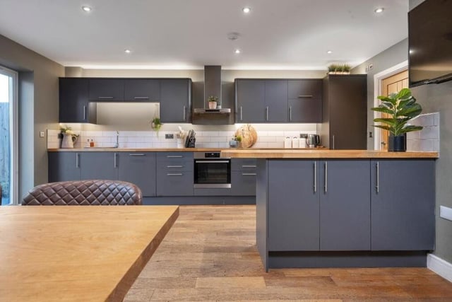 The kitchen features a modern range of subtle dark grey wall cupboards, base units and drawers, with solid wooden work surfaces over. At the heart is an integrated oven and a four-ring induction hob with stainless steel extractor hood over.