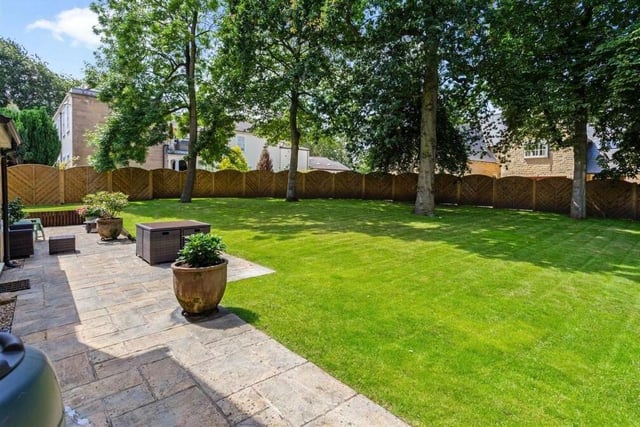 The well-maintained rear garden, bound by an arched fence, is predominantly laid to lawn, with mature trees.