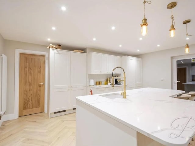 Elegant marble worktops provide a timeless centrepiece, their natural veining adding character and sophistication, while bespoke cabinetry is complemented by exquisite gold feature handles that bring a touch of opulence to the space.