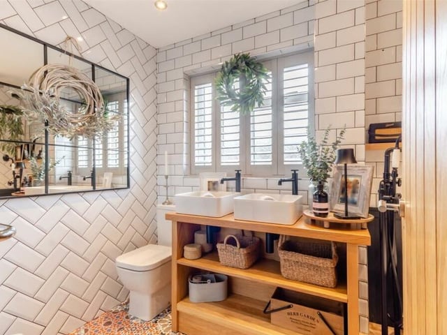 Also on the first floor of the Deepdale Park property is this superbly appointed family bathroom. Ingeniously designed, it consists of a four-piece white suite complemented by black matte and chrome fittings. This image shows the twin his and hers wash hand basins, mounted on an oak table with two rows of shelving beneath.