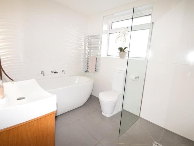 Our last photo from the Ravenshead property shows the family bathroom. Quality is not compromised in a suite comprising a double-ended bath with waterfall tap, walk-in shower with rainfall shower head, wash basin with double-drawer vanity unit and low-flush WC. The floor and walls are tiled, and there is also a chrome, heated towel-rail.