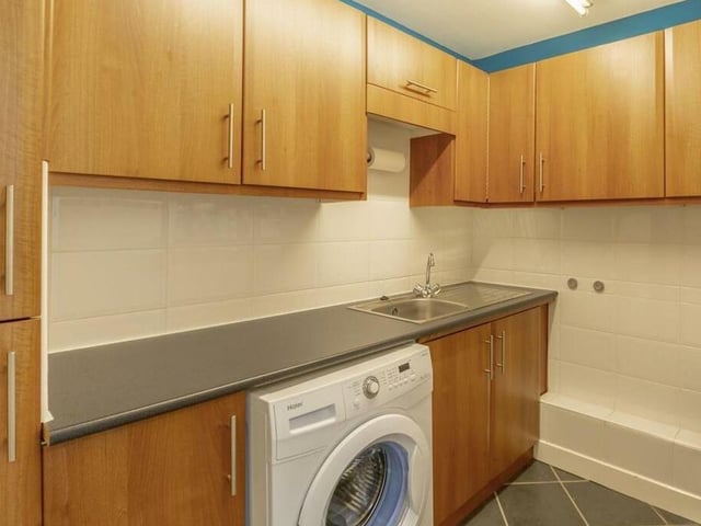 Not far from the kitchen is this handy utility room, where there is space and plumbing for a washing machine. Matching cabinets and units provide additional storage, while there is also a sink and work surface.