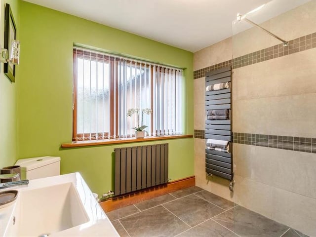 The ground floor also houses this wet room, which is beautifully appointed. It comprises a three-piece suite with chrome fittings and features a walk-in, tiled shower, vanity unit with inset wash hand basin and two storage drawers beneath, low-flush WC, heated towel-rail and tiled floor.