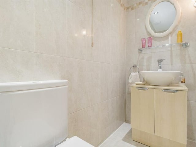 Here is the en suite to the master bedroom at the £450,000 Mansfield bungalow. A modern three-piece suite includes a vanity unit with contemporary wash hand basin and storage cupboard beneath, plus a low-flush WC. The walls and floor are tiled.
