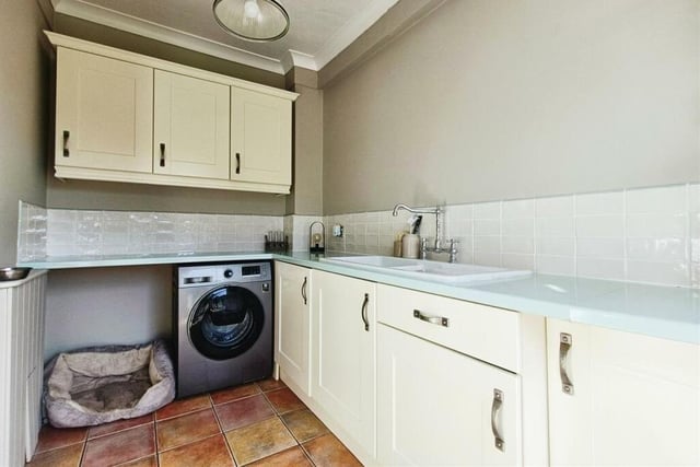 Not far from the kitchen is this handy utility room, which has space and plumbing for additional appliances, such as a washing machine. There are more shaker-style units and cabinets, and a second sink with drainer.,