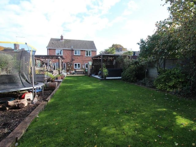 This is a view of the back of the house, with the garden including a lengthy, well-maintained lawn and, to the left, a barked play area. The garden is enclosed by timber fencing, with gated access to the side.