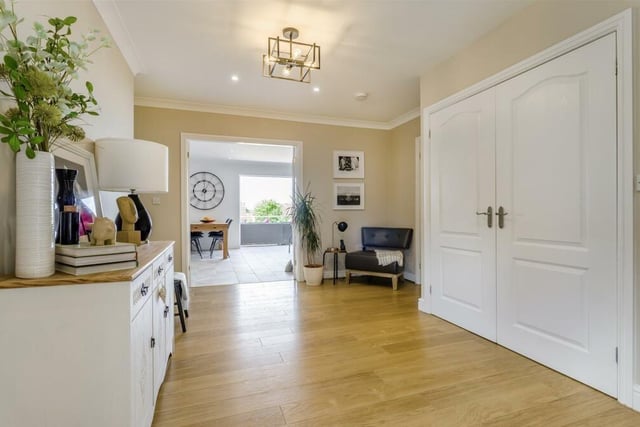 The large, L-shaped hallway has a built-in storage cupboard, a cloaks cupboard, underfloor heating, a laminate floor and ceiling spotlights. The big double doors lead to the open-plan living, dining and kitchen area.