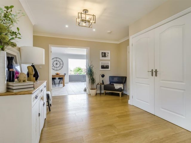 The large, L-shaped hallway has a built-in storage cupboard, a cloaks cupboard, underfloor heating, a laminate floor and ceiling spotlights. The big double doors lead to the open-plan living, dining and kitchen area.