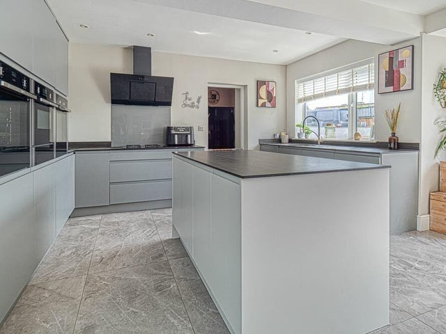 The kitchen features two integrated electric ovens, a microwave, dishwasher, sink, drainer and mixer taps, LED spotlights, a central island and a range of storage cupboards.