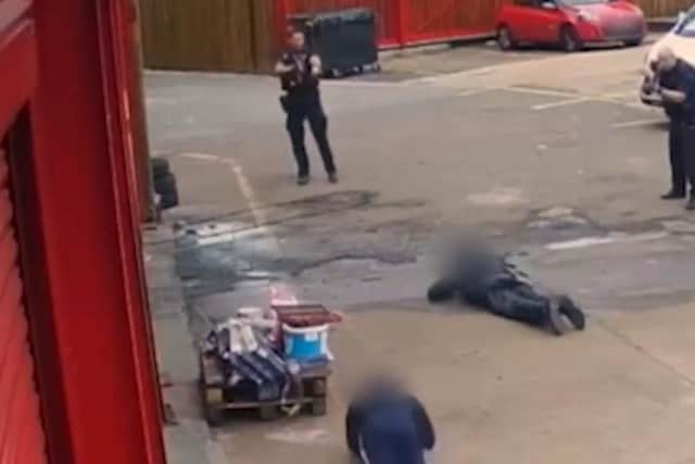 A screenshot from the video shows armed officers ordering two men to lie on the ground.