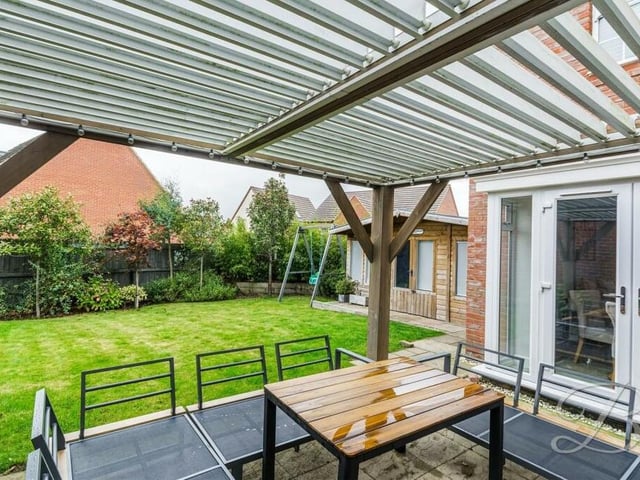 This photo takes us beneath the sheltered pergola in the back garden, looking across to a manicured lawn and planted trees.
