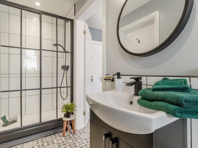 Sandwiched between the second and third bedrooms is this smart Jack and Jill en suite. It comprises a tiled shower enclosure, vanity unit with wash hand basin and storage cupboard, low-flush WC, tiled walls, ceiling spotlights and tile-effect vinyl floor.