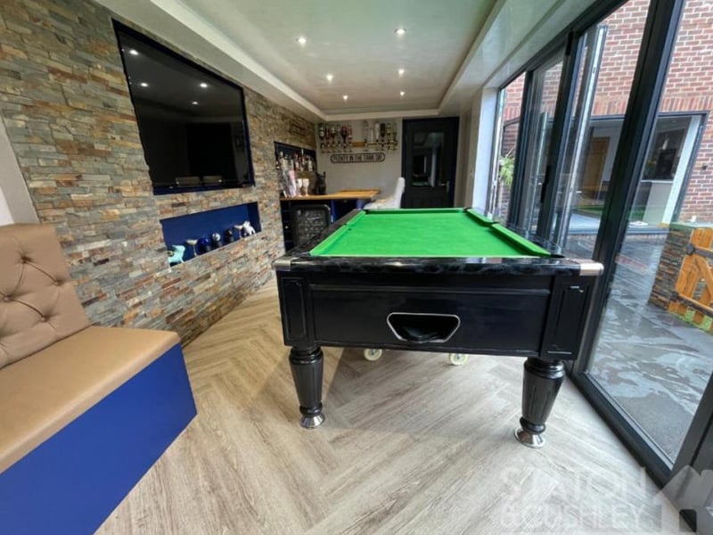 The games room from a different angle. As well as a fitted bar and shelving, it has LVT flooring, spotlights and a tiled feature wall. Large bi-folding doors open out to the exterior of the property, forming an extension to the garden during the summer.
