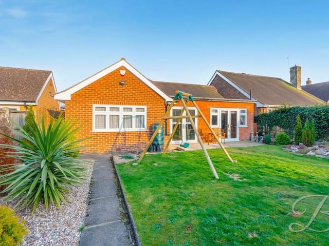 Stepping outside now and a view from the back of the bungalow. The spacious garden features a patio area for seating, a well-maintained lawn and decorative shrubs.
