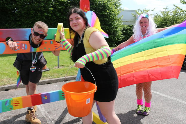 Construction and the built environment student Toni Chapman, centre, prepares to give carpentry and joinery student William Walker a soaking in the stocks, watched by youth worker Ruth Lee holding the rainbow flag.
