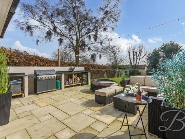 The garden also features this raised patio area, ideal for alfresco entertaining. Not only does it have a seating area but also a glass balustrade, a fitted kitchen with hot and cold water, a Belfast sink and a substantial marble worktop for preparing food. There is space for a barbecue and an outdoor fridge too.