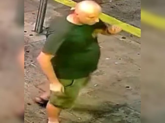 Bald man, green t-shirt with logo lefthand side of chest, khaki shorts and sandals.