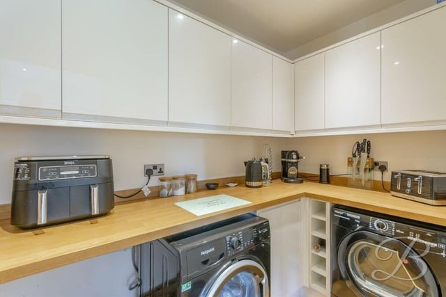 Just off the kitchen is this handy utility room, where there is space and plumbing for a washing machine and tumble dryer. It is fitted with gloss cabinets and units, plus a work surface.