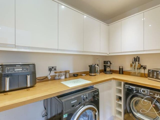 Just off the kitchen is this handy utility room, where there is space and plumbing for a washing machine and tumble dryer. It is fitted with gloss cabinets and units, plus a work surface.