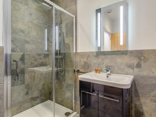 This second image of the family bathroom shows the large shower enclosure and attractive vanity unit with mirror above.