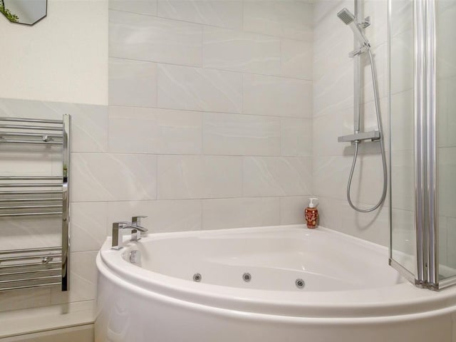 The bathroom also includes this corner Jacuzzi panelled bath with and shower over and mixer tap.