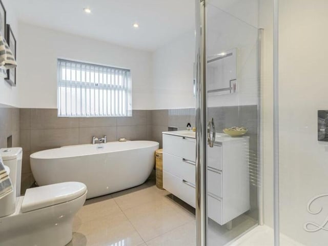 Completing our look at the first floor is this modern family bathroom. A white suite comprises a free-standing bath, shower cubicle with rainfall shower, wash hand basin, low-level WC, chrome, heated towel-rail, tiled floor and ceiling spotlights.