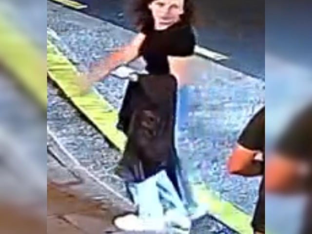 Woman with curly hair, black t-shirt and jeans, carrying a jacket.